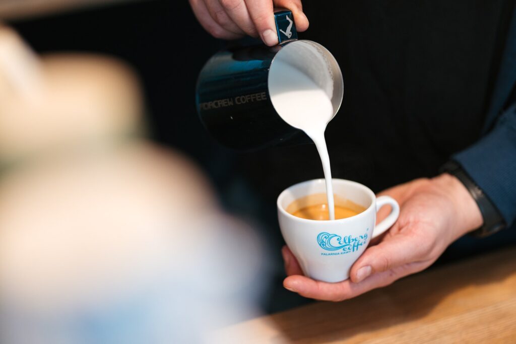 Wlewanie spienionego mleka do espresso podczas przygotowania cappuccino