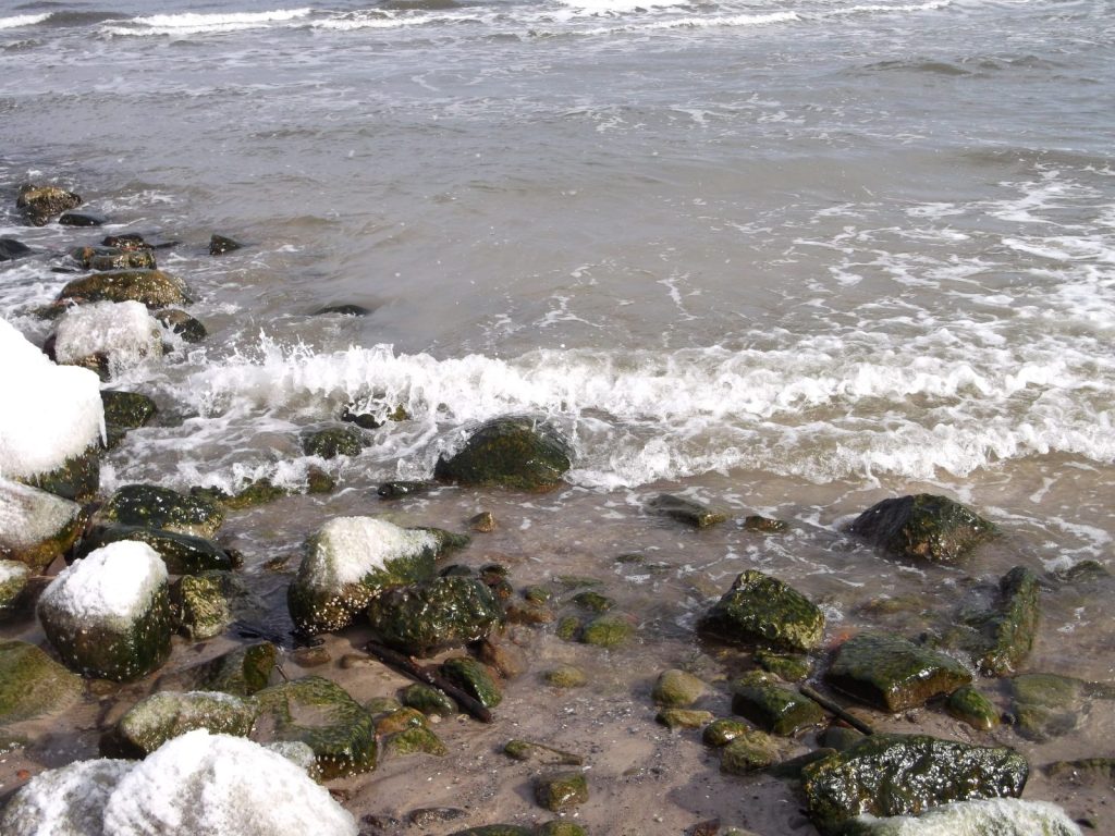 zimne fale Bałtyku i ośnieżone kamienie na plaży w Kołobrzegu