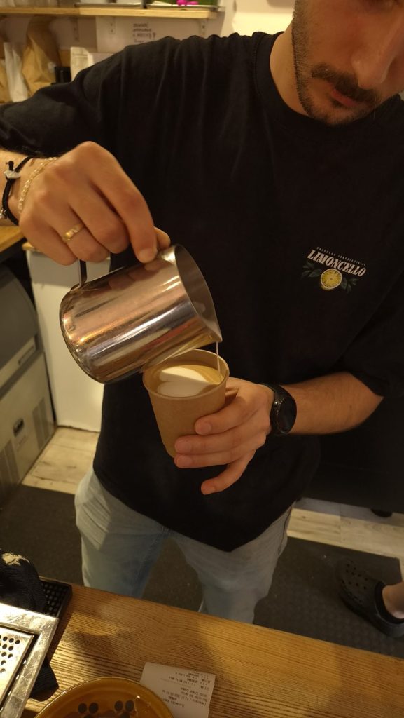 barista Colbergcoffee wlewa mleko i robi latte art w kubku na wynos